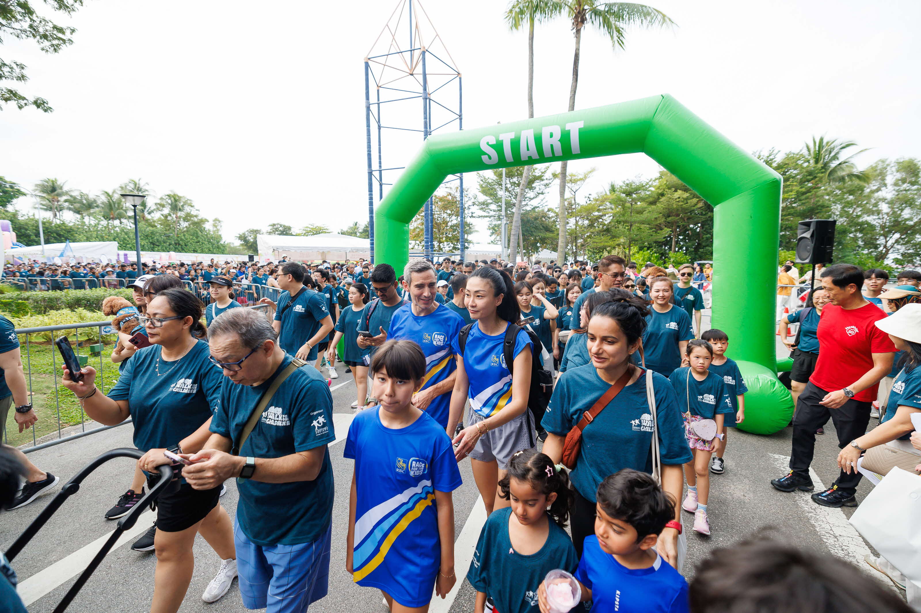 Crowd of people in matching shirts walk under a green "START" archway in a park.